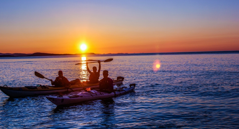 the silhouettes of people sitting in kayaks appear in front of a sunset